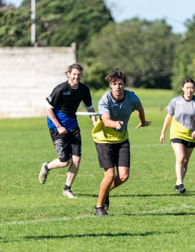 Group of five people running through a field playing frisbee